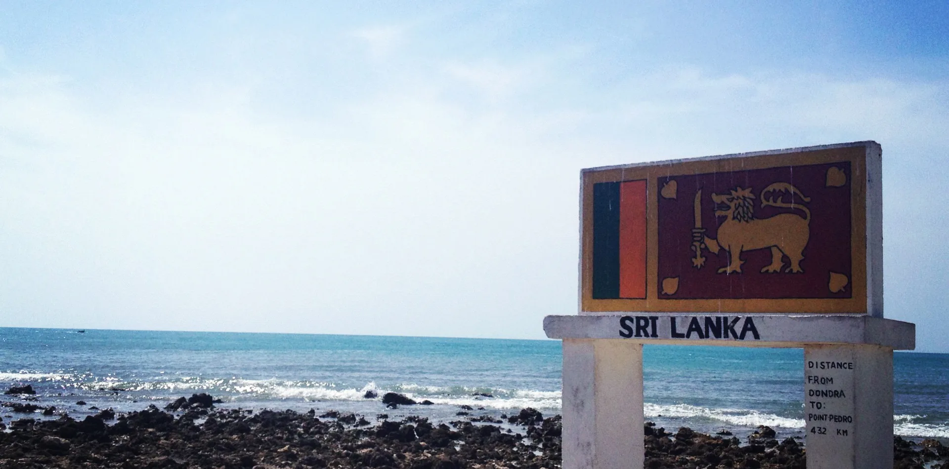 A weathered signpost marking Point Pedro on Sri Lanka's northern coast, with the Indian Ocean beyond.