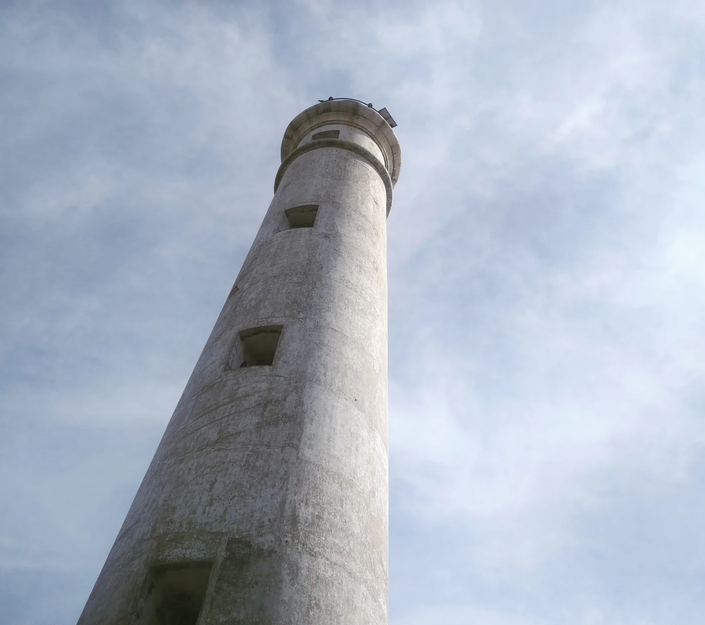 Point Pedro lighthouse, a tall white tower, viewed from below against a pale sky.