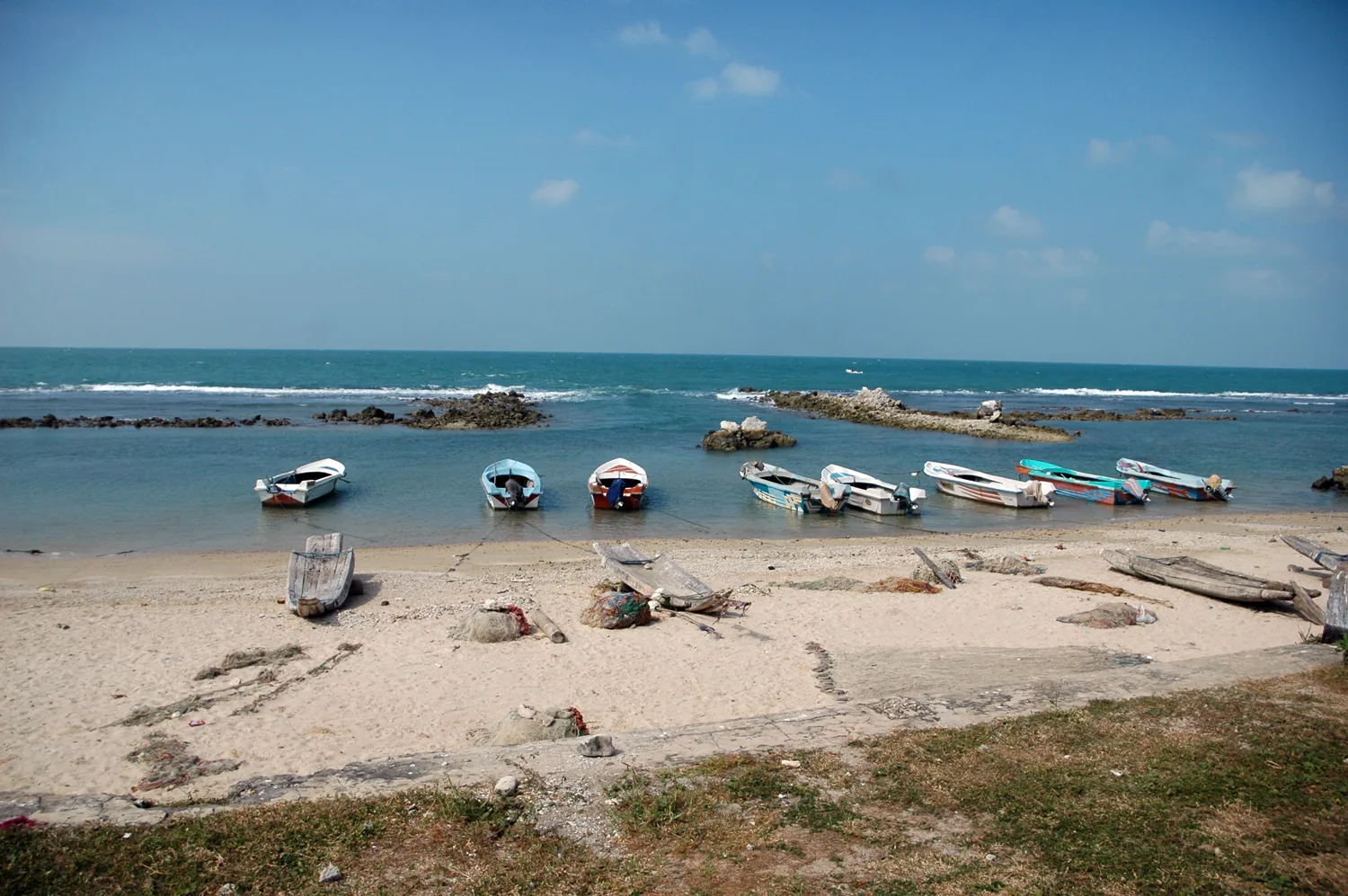 Fishing boats anchored close to shore at Valvettithurai beach under a clear sky.